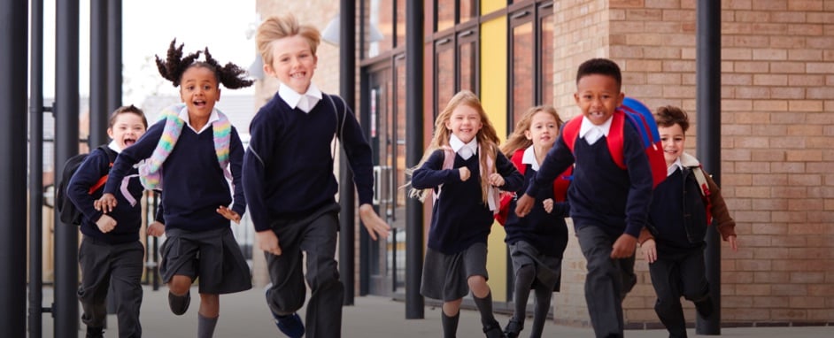 Seven school children running in a playground towards the camera.